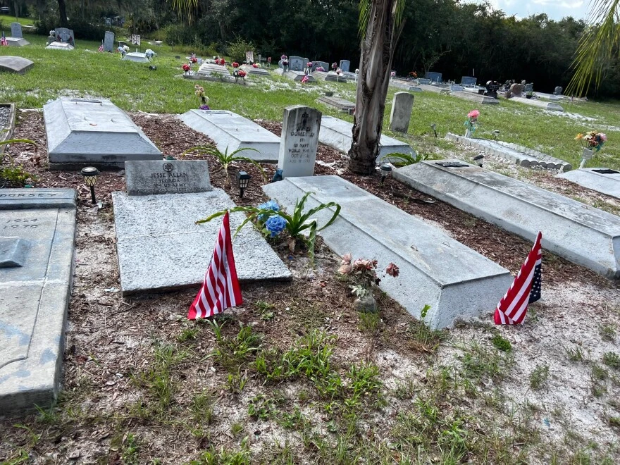 graves in a cemetery, some with American flags on the headstones