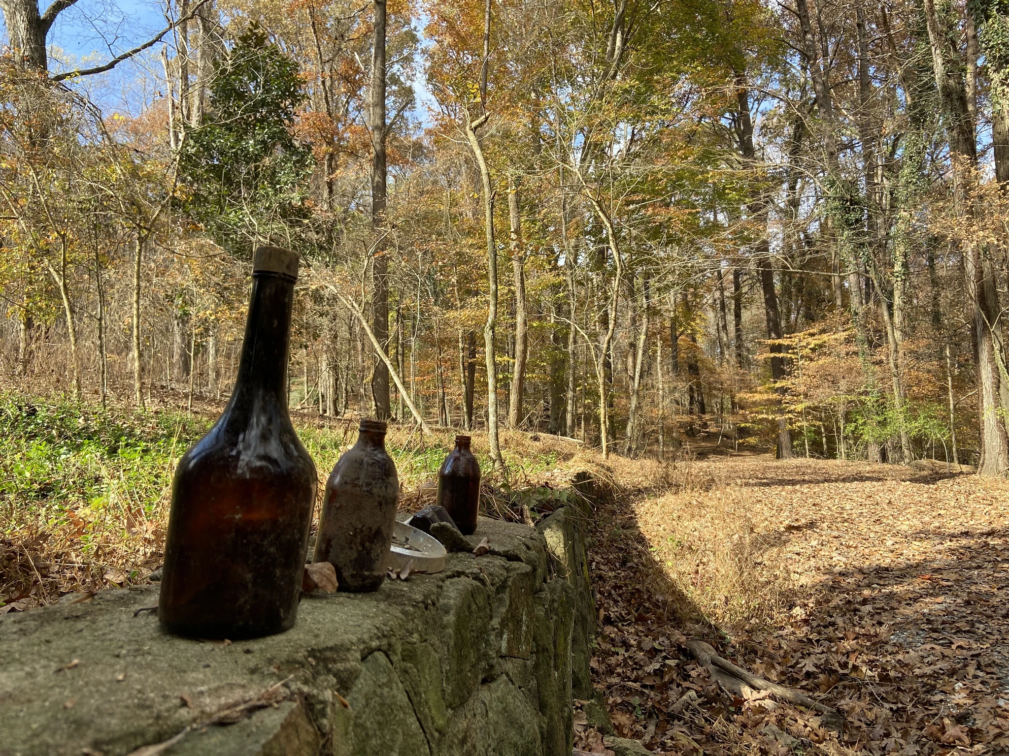 Three old bottles stand on a short stone or decorative retaining wall
