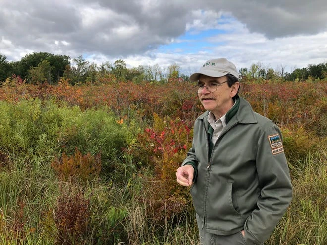 Poison ivy and its reddish hues spread behind Indiana Department of Natural Resources regional ecologist Rich Dunbar at the end of the boardwalk in the Elkhart Bog Nature Preserve.