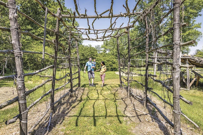 Dad next to mom holding toddler walking through Native American structure at Fort Ancient Earthworks & Nature Preserve in Oregonia Ohio