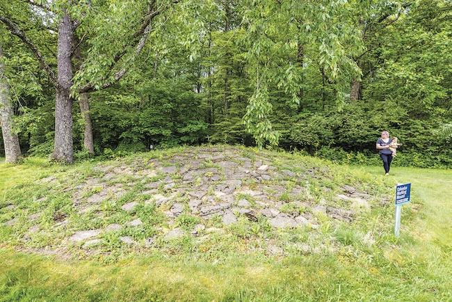 woman holding baby walking next to earthwork with dad standing and mom kneeling next to toddler inside Native American structure at Fort Ancient Earthworks & Nature Preserve in Oregonia Ohio
